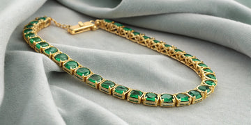 A classic emerald tennis bracelet in a yellow gold setting.