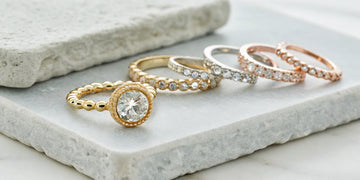 A round diamond in a gold beaded bezel ring, displayed with other wedding bands.