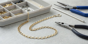 A broken gold necklace chain being assessed for repair cost with jeweler's tools nearby.