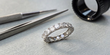 A jeweler assesses a diamond eternity band on a workbench to determine if it can be resized.