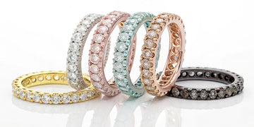 A collection of colored diamond eternity bands in pink, yellow, and blue set in gold.