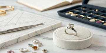 A custom engagement ring on a jeweler's workbench with design tools and loose diamonds.