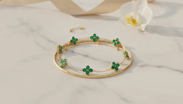 14K yellow gold emerald clover station bracelet with green emerald stations on a gold chain, styled with other gold bracelets in a layered stack