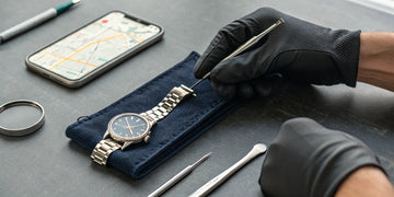 A technician performs watch maintenance services on a timepiece with precision tools.