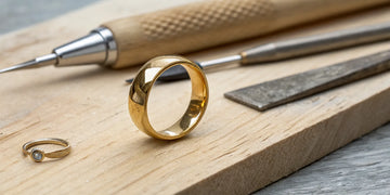 A gold ring on a jeweler's workbench with the tools needed to resize a ring smaller.