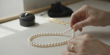 A jeweler carefully examining a pearl necklace strand on a clean work surface