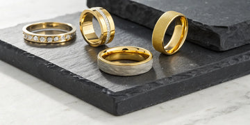 A collection of luxury men's gold wedding bands with diamond accents and unique textured finishes.