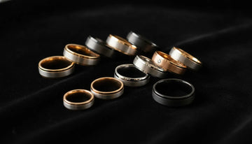 Men's wedding bands in various metals on dark velvet surface
