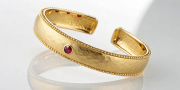 Roberto Coin gold cuff bracelet with its signature ruby and beaded edges.