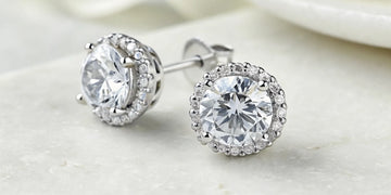 A pair of 1 carat round brilliant diamond earrings in a halo setting.