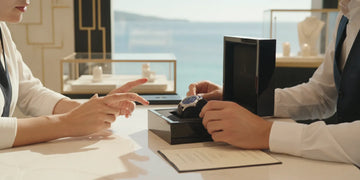 A watch owner reviewing a timepiece and its documents with a jeweler at a showroom counter