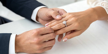 A woman's hand wearing an engagement ring on her left ring finger.