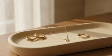 Gold necklace, hoop earrings, and rings arranged on a neutral jewelry tray