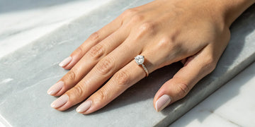 A lady's diamond engagement ring on her left ring finger.