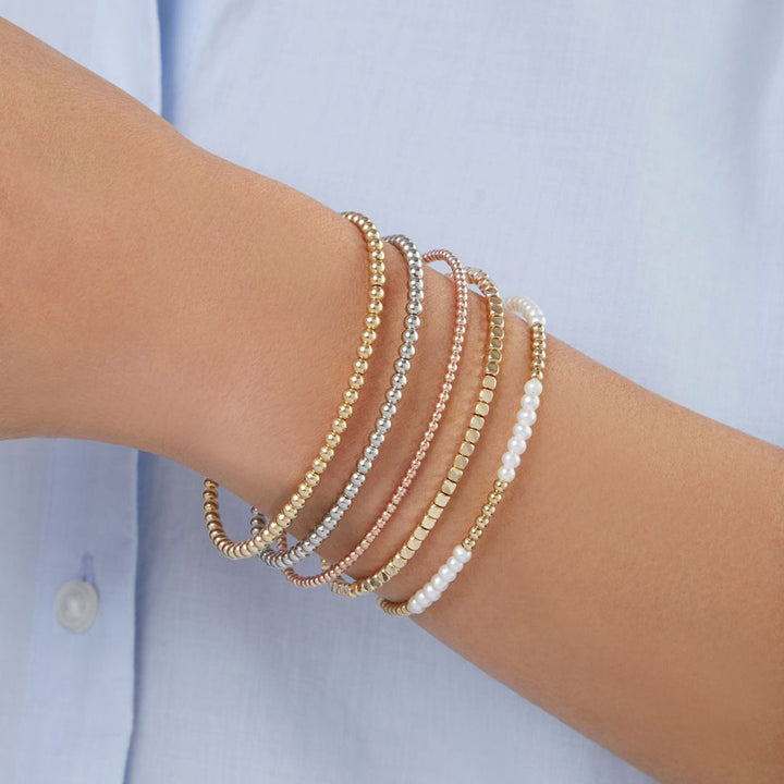 womans wrist wearing 5 beaded bracelets including a white gold beaded bracelet